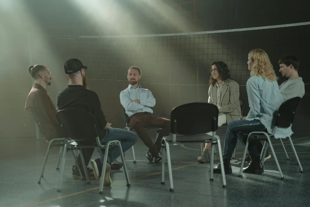 A healthcare professional takes part in a group coaching session in a gymnasium, seated in a discussion circle.