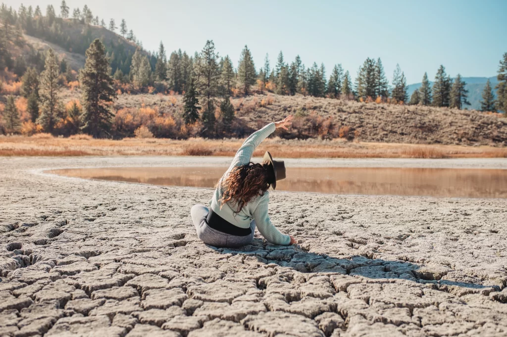 Vrouw doet yoga in de natuur bij een droog meer met bos op de achtergrond